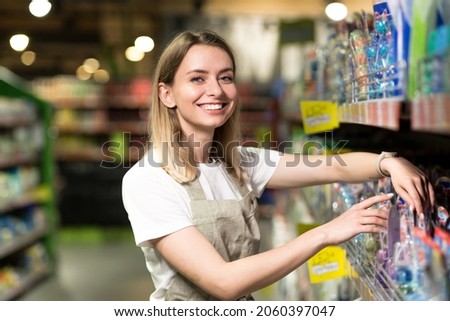 portrait of saleswoman, woman smiling and looking at camera in supermarket. Pleasant friendly female seller standing in the store between the rows . Trade business and people concept Royalty-Free Stock Photo #2060397047