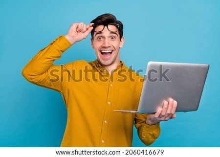Photo of excited amazed funky geek guy hold pc take off specs wear yellow shirt isolated blue color background