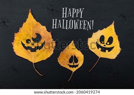 Yellow leaves with cheerful emotions on the face and black spiders on a dark background. Concept of invitation or web banner for the holiday Halloween party. Top view