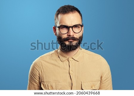 Suspicious man wears beige sweater and eyeglasses, has serious expression, tries to come up with solution. Jealous husband suspects wife in betrayal