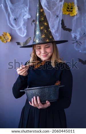 Teenage girl in a witch costume brews a potion in halloween on a gray background Royalty-Free Stock Photo #2060445011