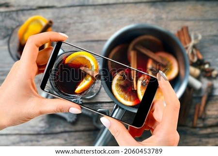 Woman takes pictures of the process of making mulled wine on a smartphone. Culinary blog or blogging concept.
