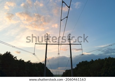 Dark silhouette of high voltage tower with electric power lines at sunrise.