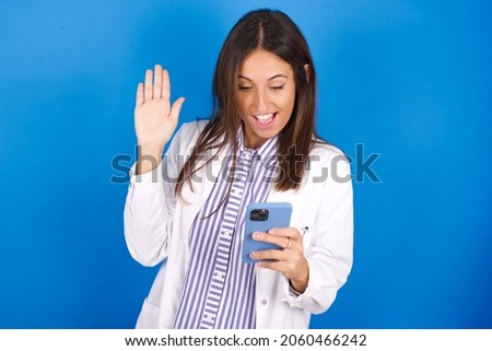 Young european doctor woman on blue background holding in hands cell reading browsing news