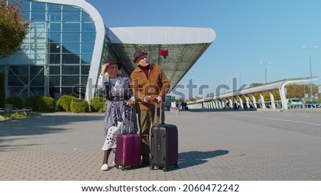 Senior couple pensioner tourists grandmother grandfather with luggage suitcases using mobile phone make selfie vlog in social media near airport hall, railway station. Travel, vacation, journey, trip