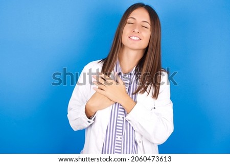 Young european doctor woman on blue background smiling with hands on chest with closed eyes and grateful gesture on face. Health concept.