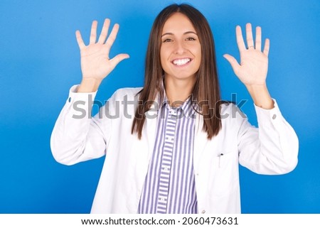Young european doctor woman on blue background showing and pointing up with fingers number ten while smiling confident and happy.