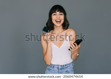 Picture of young woman holding credit card and using mobile phone over grey background