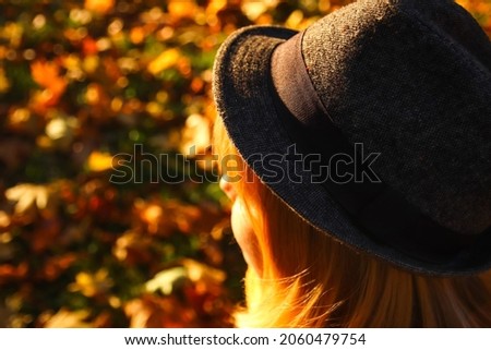Closeup back portrait of candid young Caucasian blonde woman in colorful autumn park. Bright dark stylish woman in hat and shawl of neck on fall background. Happy fall dreaming waiting concept.