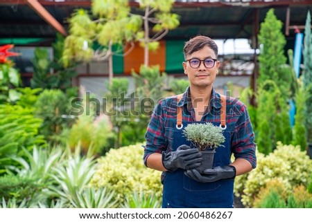 Portrait of Asian man gardener caring potted plants and flowers in greenhouse garden. Male plant shop owner working with houseplants in store. Small business entrepreneur and plant caring concept