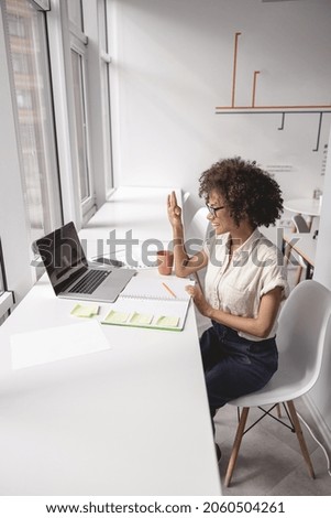 Young multiethnic lady having video call and communicating with deaf language at office