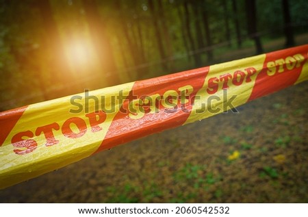 Prohibition concept. A yellow-red ribbon with the inscription Stop is hung against the background of the forest.