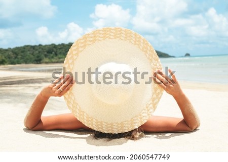 Girl lies on the white sand on the beach. Woman tanning relaxing on beach. Female adult from the back lying down with straw hat sunbathing under the tropical sun