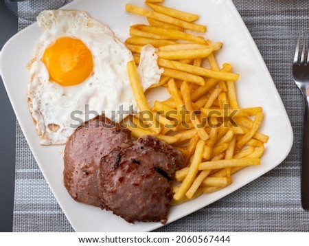 Spanish cuisine, roasted meat cutlet with fried potato and eggs on a white plate