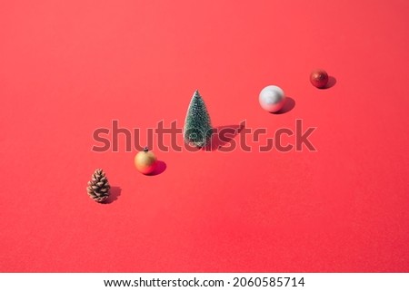 Arranged New Year and Christmas tree with yellow gold, silver, red  bauble and brown pinecone on a red pastel background. Pattern.