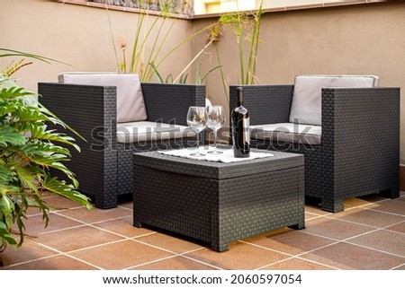 Still life view of outdoors terrace. Relaxing and lounging area with two armchair and bottle of wine on wicker table.