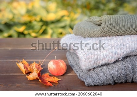 Folded autumn and winter clothing. Pile of knitted cashmere sweaters with maple leaf and apple on wooden table. Autumn composition on nature background. High quality photo