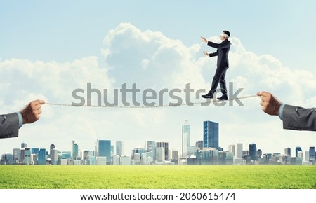 Businessman with blindfolder on eyes walking on rope over cityscape background