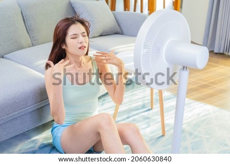 asian unhappy woman is sitting in front of working fan suffering from summer heat at home Royalty-Free Stock Photo #2060630840