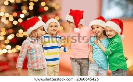 childhood, winter holidays and friendship concept - group of happy smiling little children in santa hats hugging over christmas tree lights background