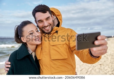 technology, relationships and people concept - happy couple with smartphone on autumn beach