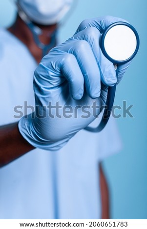 Close up of assistant hand holding stethoscope and wearing gloves against coronavirus pandemic. Nurse with uniform having medical cardiology instrument for heartbeat examination. Royalty-Free Stock Photo #2060651783