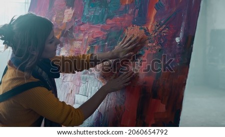 Isolated Contemporary Caucasian Female Painter Painting a Modern Art Piece. Artist Using Her Hands To Paint an Abstract Painting, Working in an Old Abandoned Warehouse. Beautiful and Colourful Art.