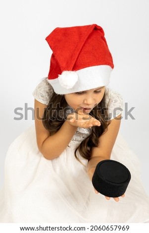portrait of gentle, joyful girl in Santa Claus hat blows a kiss to smart music speaker, isolated on white background, concept of children New Year gift. 