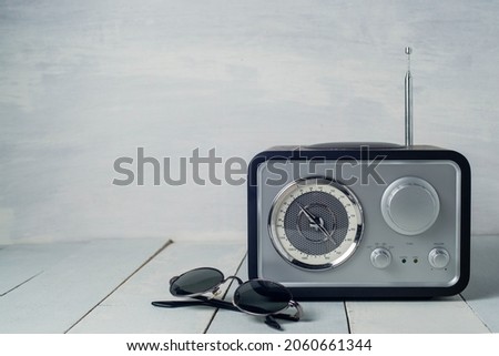 Vintage radio with flower in white vase, a blue book, a pen and sunglasses.