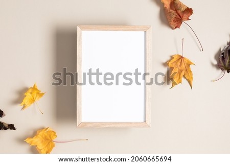 Empty wooden mockup photo frame and autumn leaves on beige background. Flat lay, top view, copy space