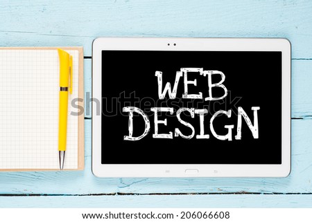 Tablet PC with text web design on wooden background with notepad and pen