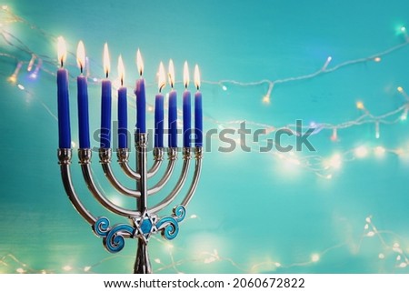 Image of jewish holiday Hanukkah with menorah (traditional candelabra) and candles over garland glitter lights background
