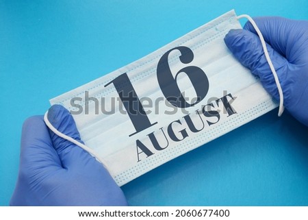 16 august day of month. Doctor holding an antivirus mask in blue medical gloves on a blue background. Protection from disease