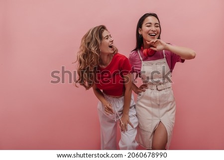 Young caucasian lady laughs hard with her pretty asian girlfriend against pink background. Image of 20s girls pretending dancing to music and having fun with each other in studio. Royalty-Free Stock Photo #2060678990