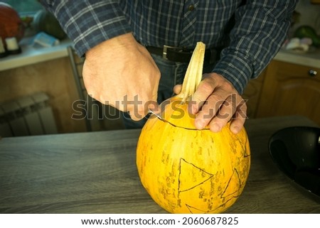 Halloween. How to make Jack O'Lantern at home? Male hands with knife, leftovers of pumpkin on the kitchen table. Selective focus and bokeh.