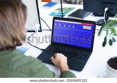 Caucasian businesswoman sitting at desk, using laptop with statistical data on screen. business communication and digital interface technology digital composite image.