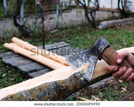grinding off the bark of an ash log by a carpenter using a sharp ax, peeling off a layer of bark from a tree trunk manually with a hatchet, processing fresh ash trunks for preparation of construction  Royalty-Free Stock Photo #2060689490