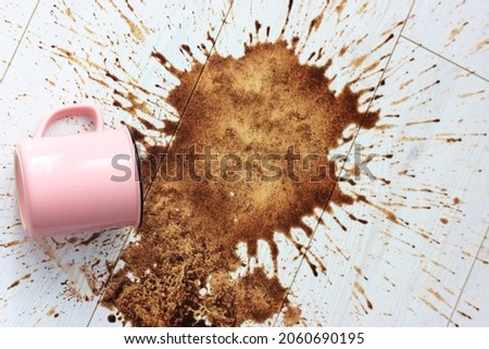 A pink ceramic mug, cup fell on a white wooden parquet floor and left a big stain on it. Spilled coffee in the morning. Lots of hot coffee drink brown splashes flying in different directions flatly.  Royalty-Free Stock Photo #2060690195
