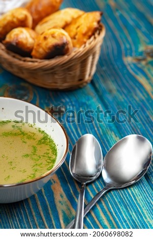 chicken broth in white bowl and baked pies in a basket on blue wooden desk