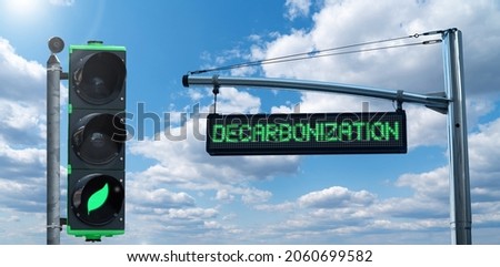 Traffic light with leaf symbol and road information board with text DECARBONIZATION on a background of blue sky. Carbon neutrality concept	