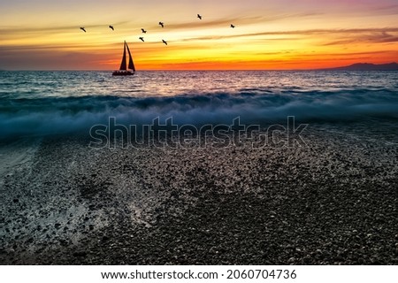 A Sailboat Is Sailing Along The Ocean Against A Colorful Sunset Sky With Birds Flying Overhead Royalty-Free Stock Photo #2060704736