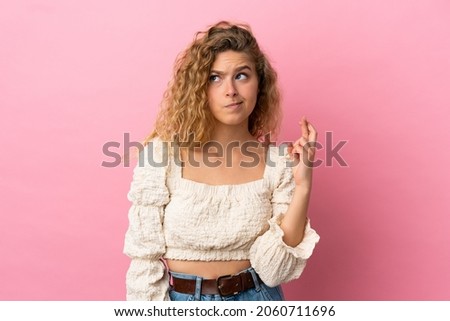 Young blonde woman isolated on pink background with fingers crossing and wishing the best