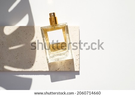 Transparent bottle of perfume with white label on stone plate on a white background. Fragrance presentation with daylight. Trending concept in natural materials with palm leaf shadows. Royalty-Free Stock Photo #2060714660