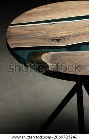 Expensive vintage furniture. The table is covered with epoxy resin and varnished. Luxury quality wood processing. Wooden table on a dark background. A blue epoxy river in a round tree slab.