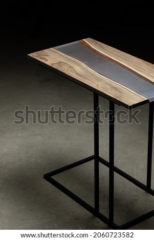 Expensive vintage furniture. The table is covered with epoxy resin and varnished. Luxury quality wood processing. Wooden table on a concrete background. A purple epoxy river in a rectangular tree slab
