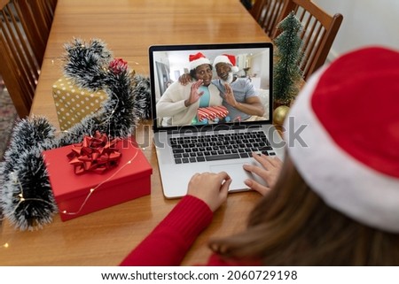 Caucasian woman making laptop christmas video call with waving african american senior couple. christmas, festivity and communication technology.