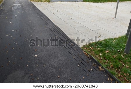 asphalt street surface with grooves for the blind. the sidewalk has several milled grooves for water drainage and emphasis on the end of one part and the beginning of the other for blind citizens