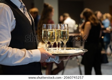 A waiter is holding a plate with sparkling wine to welcome people at an event. Glasses with champagne to toast. Drinks at a luxury party in a hotel. Royalty-Free Stock Photo #2060745257