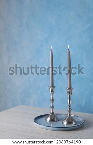 Holders with burning candles on wooden table near light blue wall, space for text