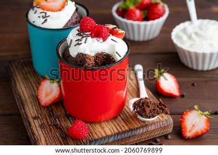 Chocolate mug cake with whipped cream and fresh berries on a dark wooden background. Cupcake cooked in the microwave Royalty-Free Stock Photo #2060769899